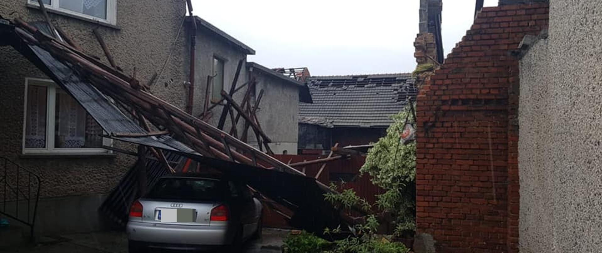 Zdjęcie przedstawia zerwany dach stodoły, który zatrzymał się na samochodzie osobowym na posesji u sąsiada.