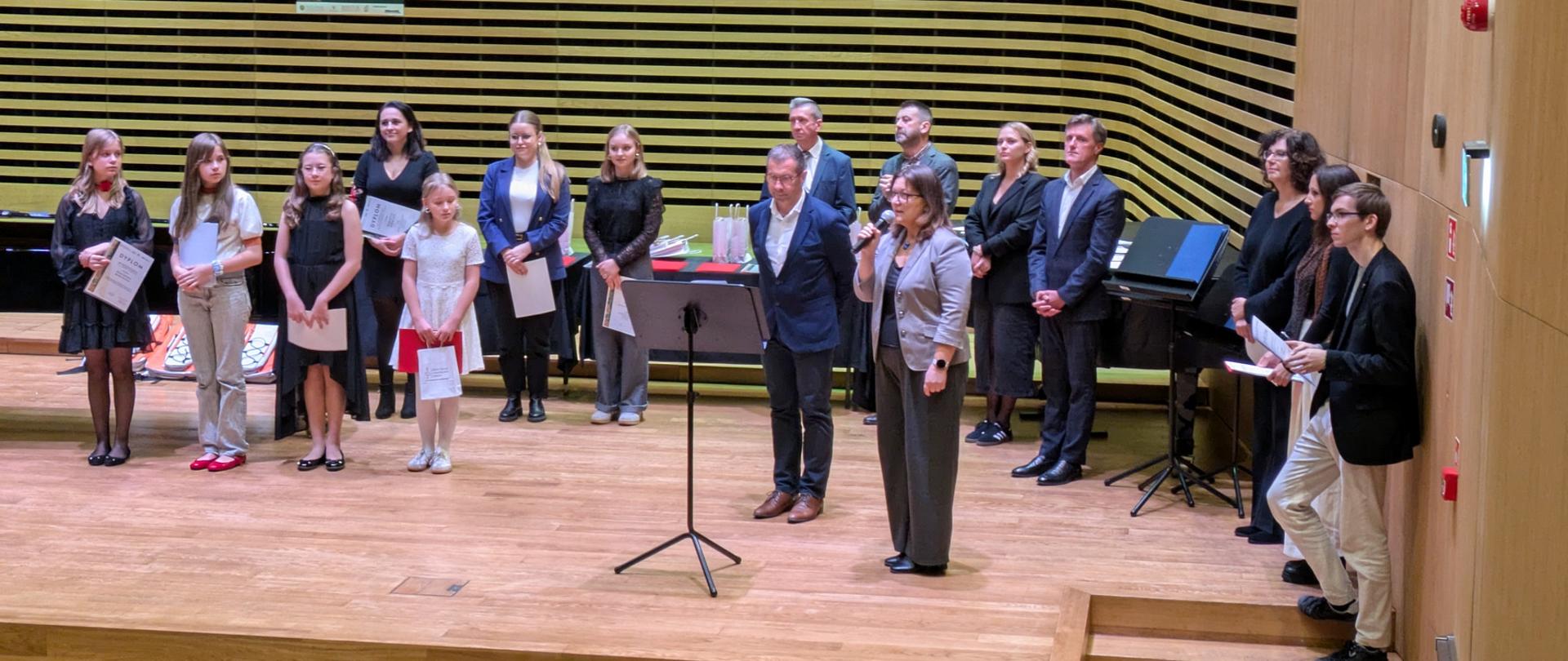 Jury i Dyrekcja szkoły wręczają na estradzie sali koncertowej nagrody Laureatom.