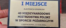 Na zdjęciu widoczna jest tabliczka z pucharu na której widnieje napis " 1 MIEJSCE KLASYFIKACJA GENERALNA 40 MIĘDZYNARODOWE MISTRZOSTWA POLSKI W SPORCIE POŻARNICZYM CZĘSTOCHOWA 13-14.06.2024 R.".