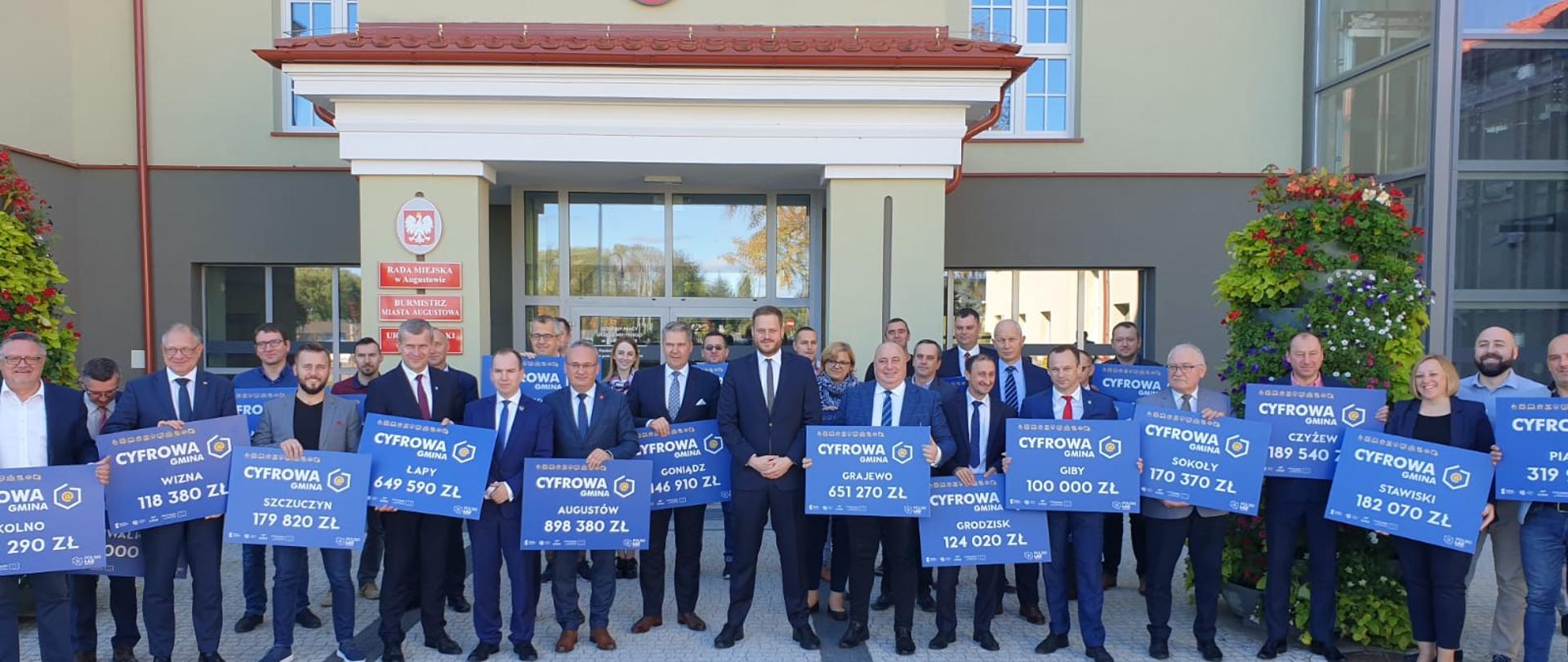 Zdjęcie ministrów Janusza Cieszyńskiego i Adama Andruszkiewicza z samorządowcami przed urzędem miejskim w Augustowie.