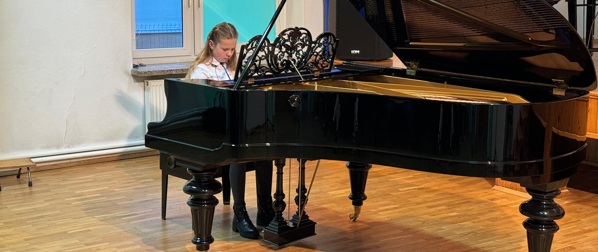 Zdjęcie przedstawiające jednego z uczestników koncertu przy fortepianie w auli szkoły.