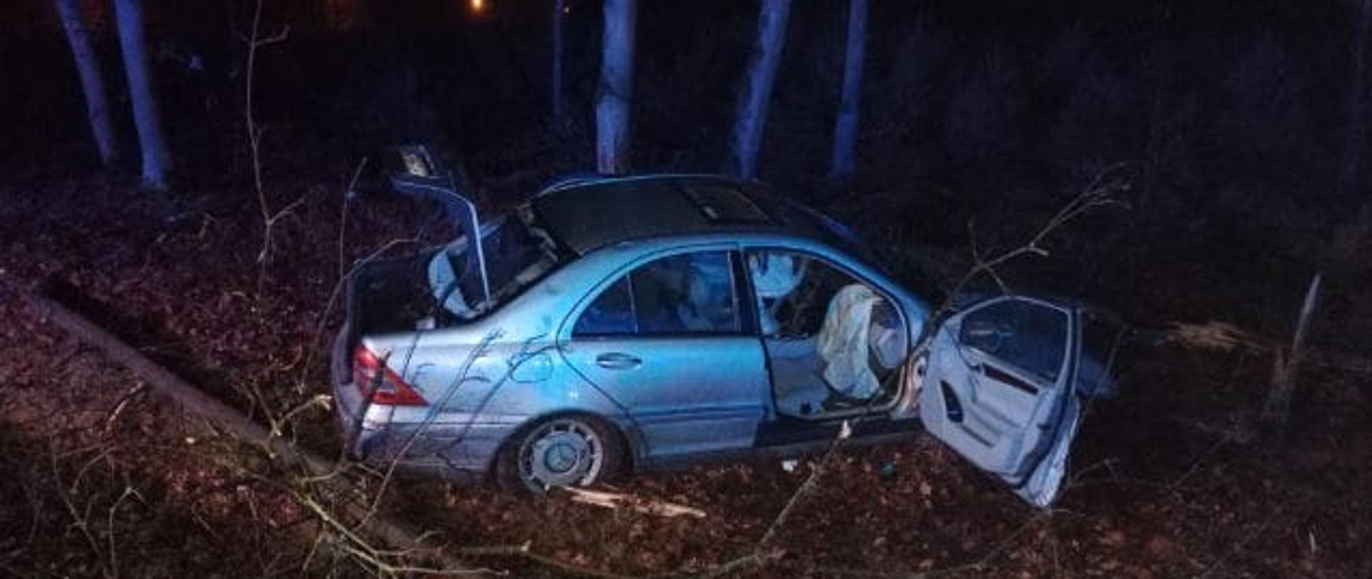 Widać uszkodzony samochód od strony pasażera, jest noc