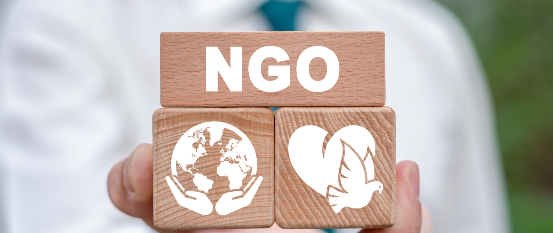 Klocki drewniane z napisem NGO, pod spodem ikona świata, a po prawej ikona gołębia z sercem