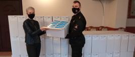 Zdjęcie przedstawia symboliczne przekazanie przez p.o. Zastępcę Komendanta Powiatowego PSP w Gołdapi kpt. Michała Herman kartonu z 1000 szt. maseczek ochronnych dla Kierownik wydziału ds. administracyjnych UM w Gołdapi Pani Róży Popławskiej