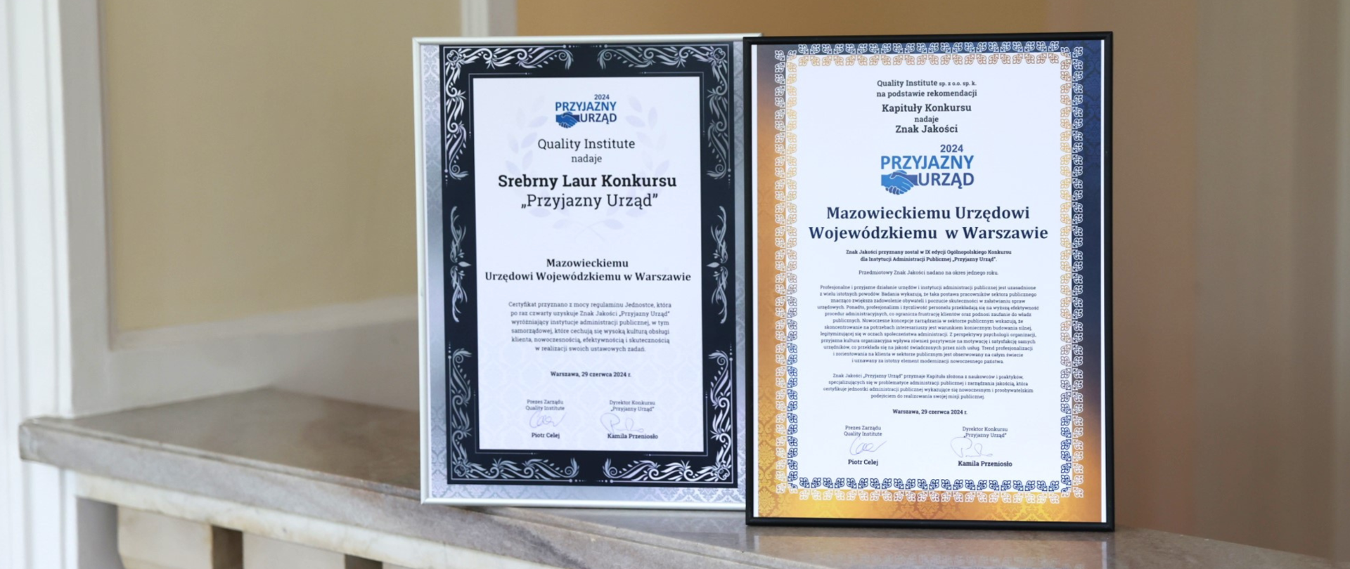 Na zdjęciu certyfikaty potwierdzające przyznanie Znaku Jakości Przyjazny Urząd i Srebrnego Laura Konkursu "Przyjazny Urząd". Dokumenty umieszczono obok siebie na marmurowym postumencie. Oprawione zostały w ramki. 