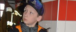 Eliminacje powiatowe OTWP. Garaż wozów bojowych. Uczestnik eliminacji odpowiada na pytania dotyczące sprzętu ratowniczego. W rękach trzyma siodełko wężowe. W tle ubrania specjalne. 