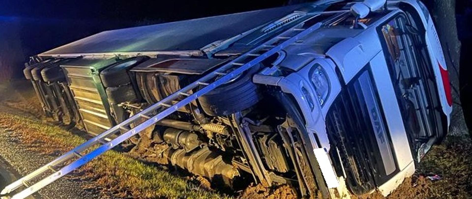 na zdjęciu widać samochód ciężarowy TIR w rowie na boku poza drogą, drabina pożarnicza przystawiona do kabiny pojazdu, na drodze wozy strażackie.