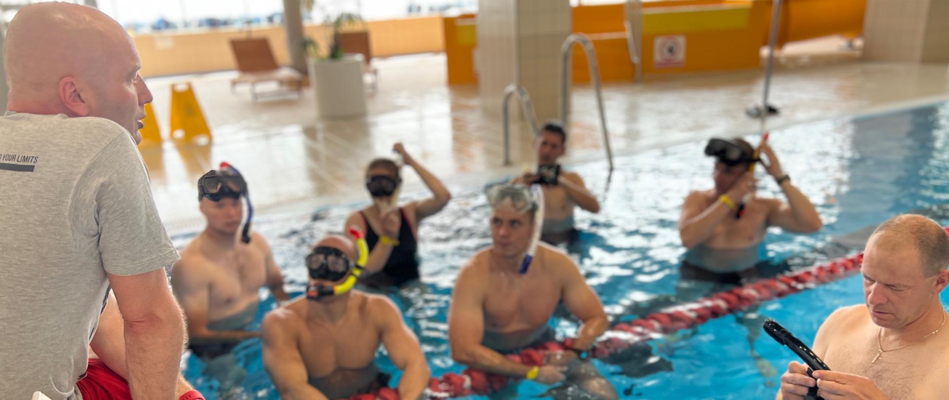 na zdjęciu strażacy z maskami i fajkami w basenie 