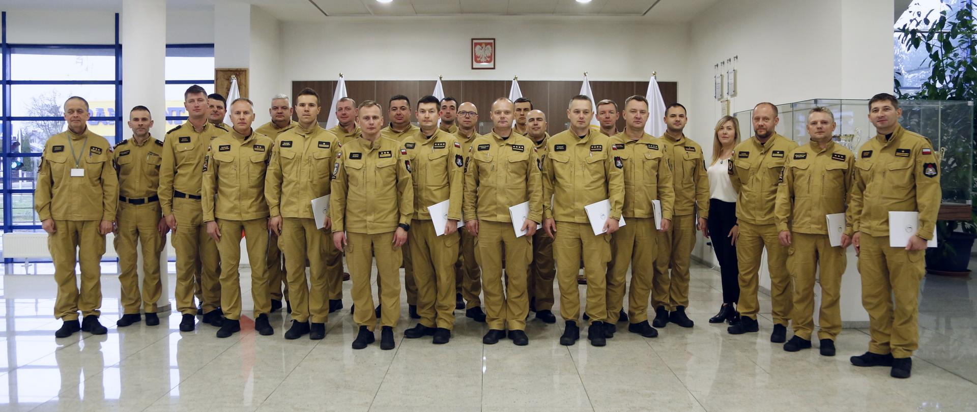 Grupowe zdjęcie funkcjonariuszy PSP (19 osób) będących uczestnikami szkolenia w towarzystwie Zastępcy Komendanta Centralnej Szkoły PSP, trzech oficerów CS PSP oraz kobiety
