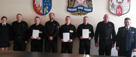 Na zdjęciu widać pełniącego obowiązki komendanta miejskiego Państwowej Straży Pożarnej w Radomiu st. bryg. Marcina Ziomka w asyście dowódców jednostek ratowniczo – gaśniczych oraz funkcjonariuszki wydziału kadr komendy miejskiej. Komendant oraz funkcjonariuszka ubrani są w mundury galowe. Kadra dowódcza w ubrania dowódczo - sztabowe w kolorze czarnym. Pomiędzy nimi stoją trzej nowo przyjęci do służby funkcjonariuszy. Strażacy ustawieni są w rzędzie jeden obok drugiego. W rękach trzymają akty przyjęcia do służby. Ubrani są w czarne ubrania koszarowe z jaskrawymi elementami odblaskowymi. Zdjęcie wykona w sali konferencyjnej Komendy Miejskiej Państwowej Straży Pożarnej w Radomiu. 