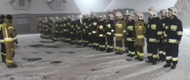 Na placu Komendy Powiatowej Państwowej Straży Pożarnej w Świeciu w dwuszeregu stoją druhowie ochotniczych straży pożarnych biorący udział w w szkoleniu podstawowym. Przed nimi stoją dwaj strażacy, którzy omawiają przebieg egzaminu. 