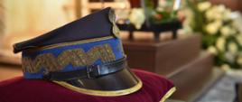 Czapka wyjściowa generalska spoczywa na czerwonej poduszce. Obok niej na katafalku stoi urna z prochami zmarłego generała Państwowej Straży Pożarnej.