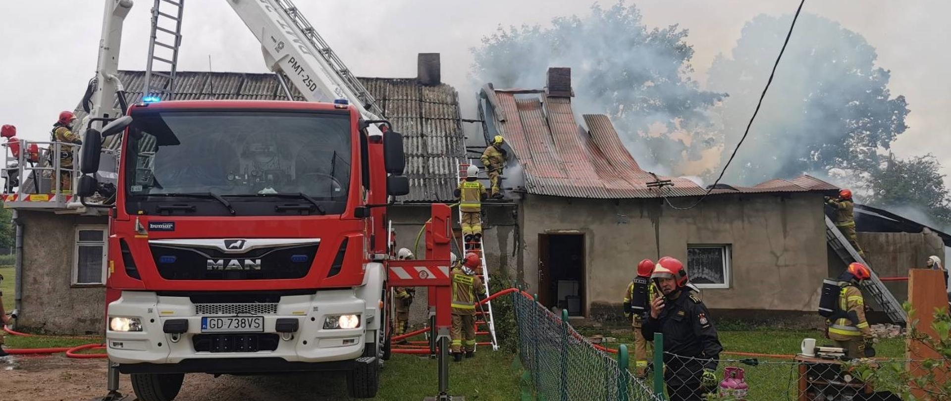 Samochód specjalny z podnośnikiem rozstawiony przed budynkiem objętym pożarem. Wokoło strażacy prowadzący działania gaśnicze.
