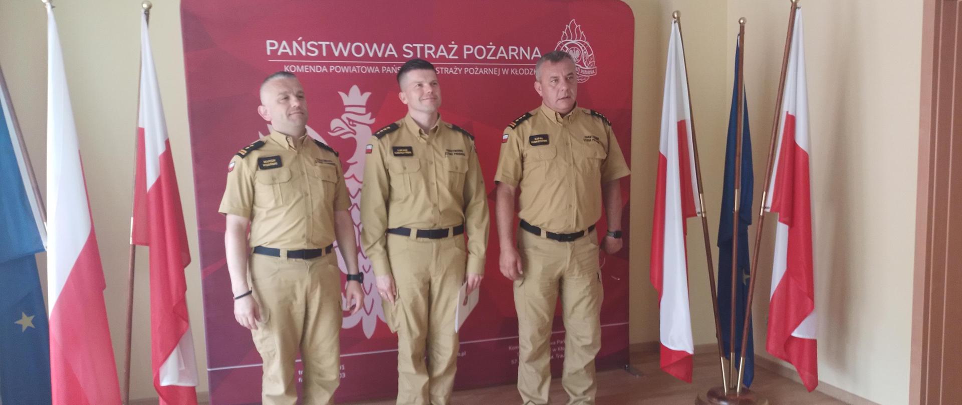 Trzech funkcjonariuszy Państwowej Straży Pożarnej pozujących do zdjęcia.