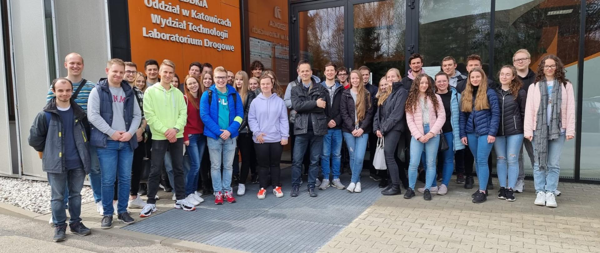 Zdjęcie grupy studentów na tle budynku laboratorium drogowego GDDKiA w Jaworznie.