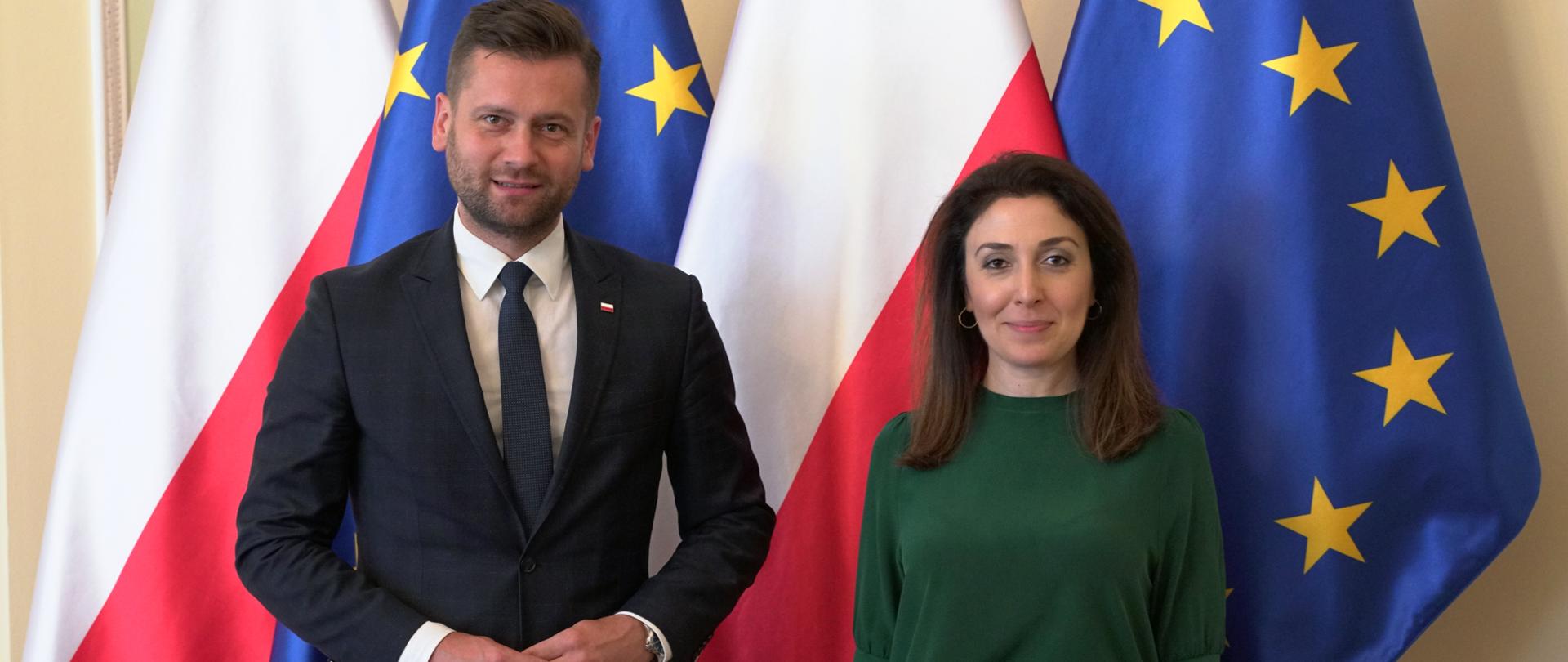 Minister Kamil Bortniczuk spotkał się z Ambasador Azerbejdżanu Nargiz Gurbanovą. Minister i pani ambasador stoją na pierwszym planie, w tle flaga polski i Unii Europejskiej