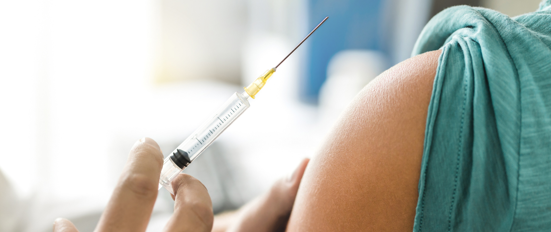 Moment szczepienia. Widoczny fragment ramienia osoby szczepionej i dłoni trzymającej strzykawkę. 