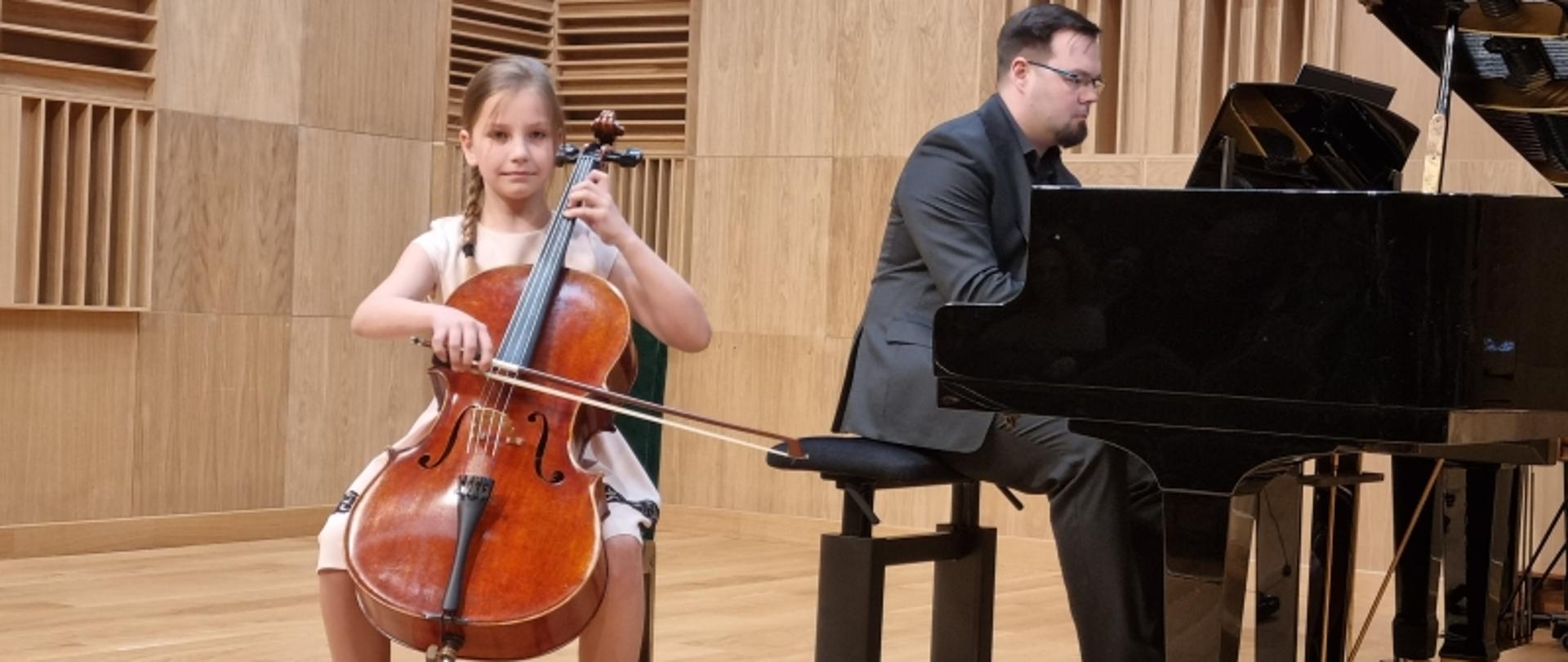 Młoda wiolonczelistka z towarzyszeniem fortepianu na estradzie.