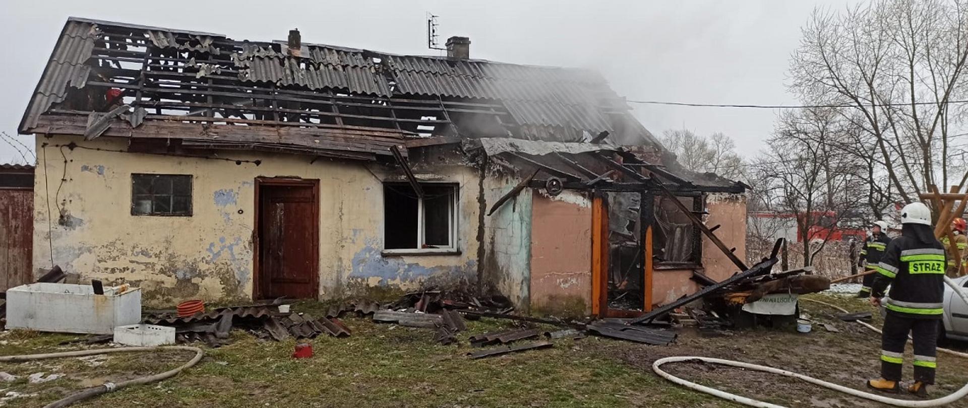 Zdjęcie przedstawia strażaka podającego prąd wody na palący się dom