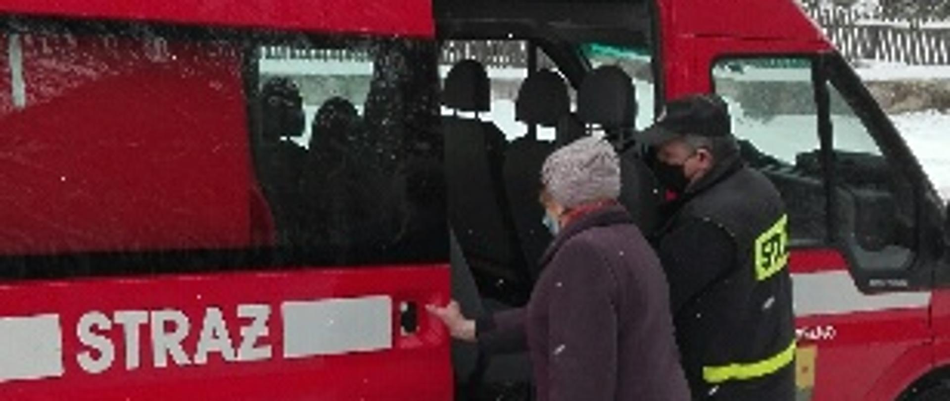 Strażak pomaga wejść do samochodu strażackiego starszej kobiecie
