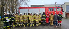 Ćwiczenia wielostanowiskowe. Grupa strażaków podczas ćwiczeń, pozuje do pamiątkowego zdjęcia na tle samochodu strażackiego. 
