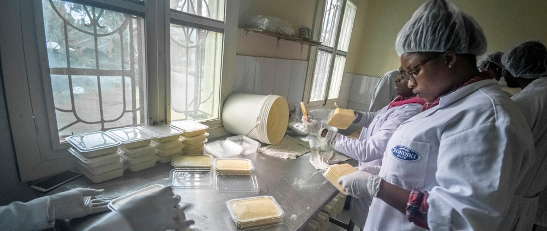 Kobiety w fartuchach i siatkach na włosach pakują masło do pojemników.