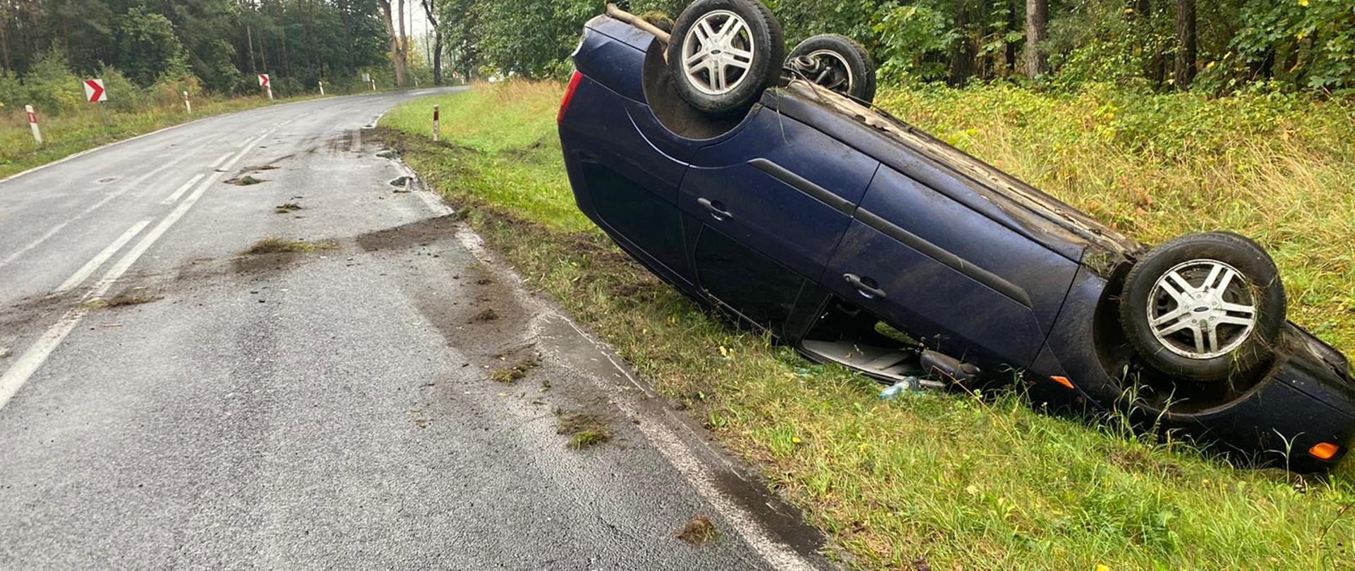 Granatowy Ford leżący na poboczu na dachu