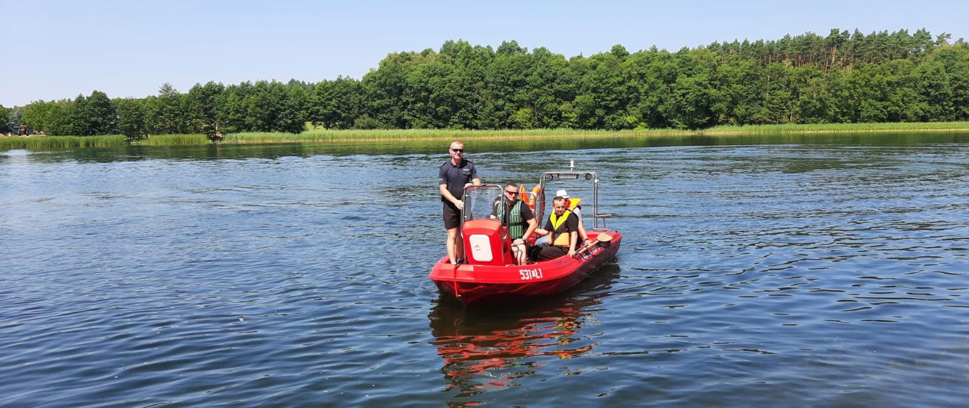 Na jeziorze płynie łódka skierowana dziobem do fotografa Państwowej Straży Pożarnej na której znajdują się funkcjonariusze Państwowej Straży Pożarnej i Policji.
