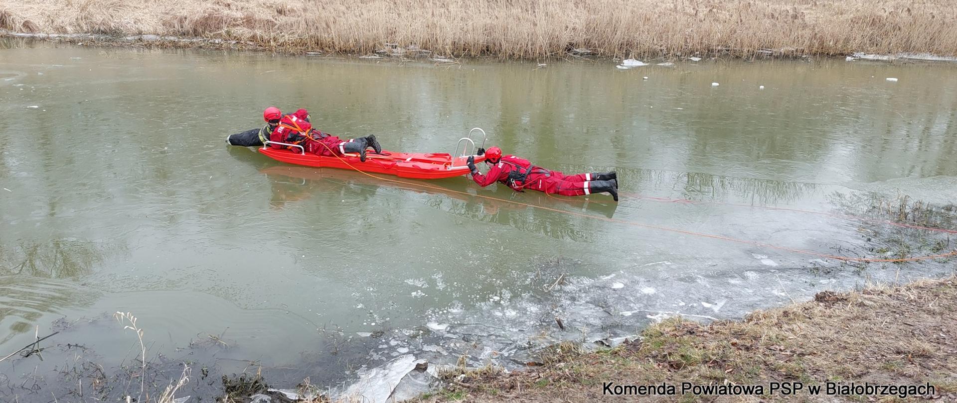 Dwóch strażaków przy pomocy sań lodowych na zamarzniętym jeziorze próbuje uratować "poszkodowanego" (manekina).