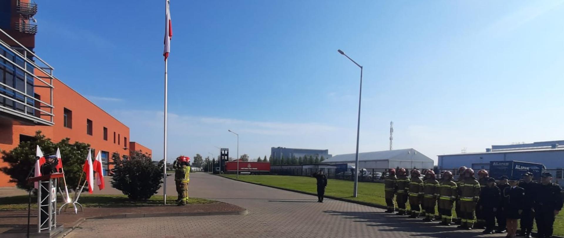 Funkcjonariusze stojący w pozycji zasadniczej podczas uroczystego wciągnięcia flagi na maszt.