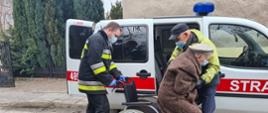 Na zdjęciu widać strażaka oraz mężczyznę pomagających zejść z wózka i wsiąść do samochodu kwatermistrzowskiego ochotniczej straży pożarnej. Kobieta i mężczyzna są spokrewnieni. W tle widać samochód kwatermistrzowski z OSP Skarżysko.
