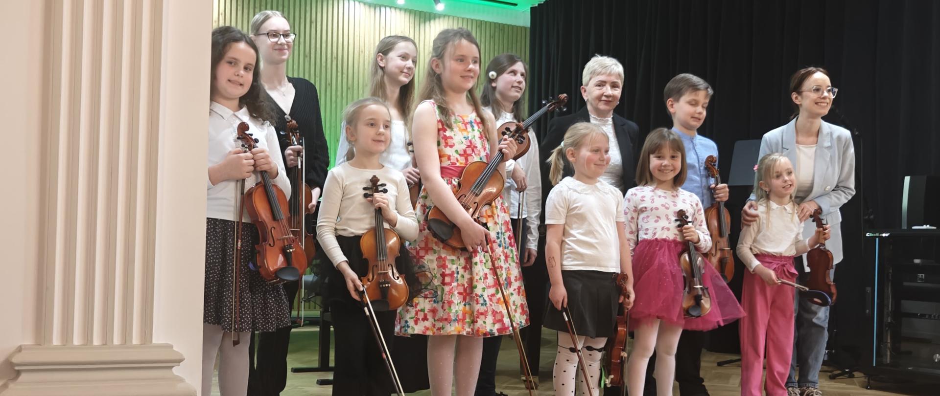 Galeria 15 zdjęć przedstawia koncert uczniów klasy skrzypiec, który odbył się w sali koncertowej Państwowej Szkoły Muzycznej I stopnia w Kłodzku. Fotografie ukazują młodych wykonawców podczas występu, ich zaangażowanie i skupienie, a także atmosferę wydarzenia oraz reakcje publiczności w kameralnej przestrzeni sali koncertowej.