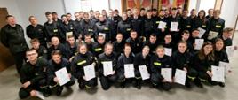 Na zdjęciu strażacy z Ochotniczych Straży Pożarnych ubrani w ubrania koszarowe koloru czarnego, zastępca komendanta powiatowego Państwowej Straży Pożarnej w Gorlicach i Prezes Zarządu Oddziału Powiatowego Związku Ochotniczych Straży Pożarnych Rzeczypospolitej Polskiej w Gorlicach ubrani w ubrania galowe koloru granatowego oraz komisja egzaminacyjna po egzaminie kończącym szkolenie podstawowe strażaków ratowników OSP w sali konferencyjnej w Komendzie Powiatowej Państwowej Straży Pożarnej w Gorlicach. 