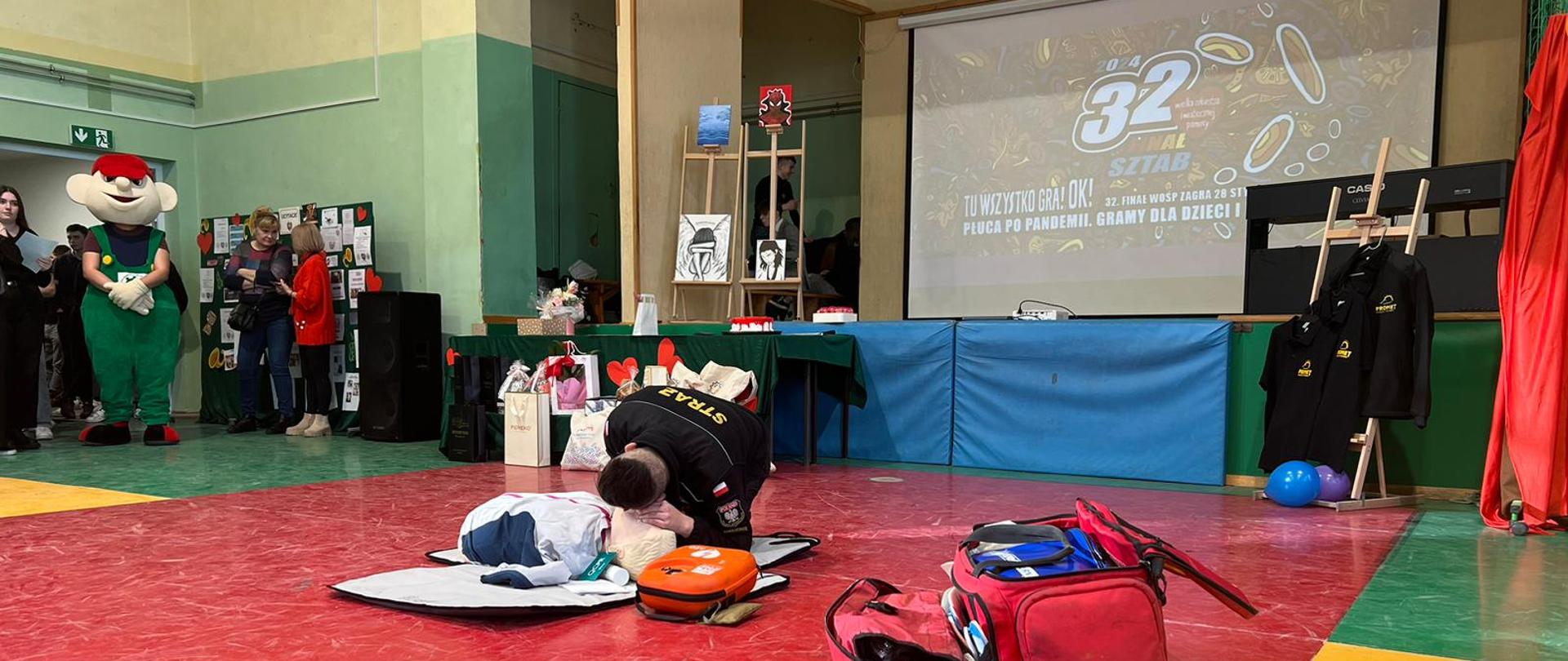 Strażak prezentujący ratownictwo medyczne na fantomie, w tle folder z z 32 finału WOŚP