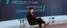 Iwona Szelenbaum z Kancelarii Prezesa Rady Ministrów siedzi na krześle i prowadzi panel dyskusyjny. W tle napis: The future is data. Przyszłość to dane. Konferencja o otwartych danych.