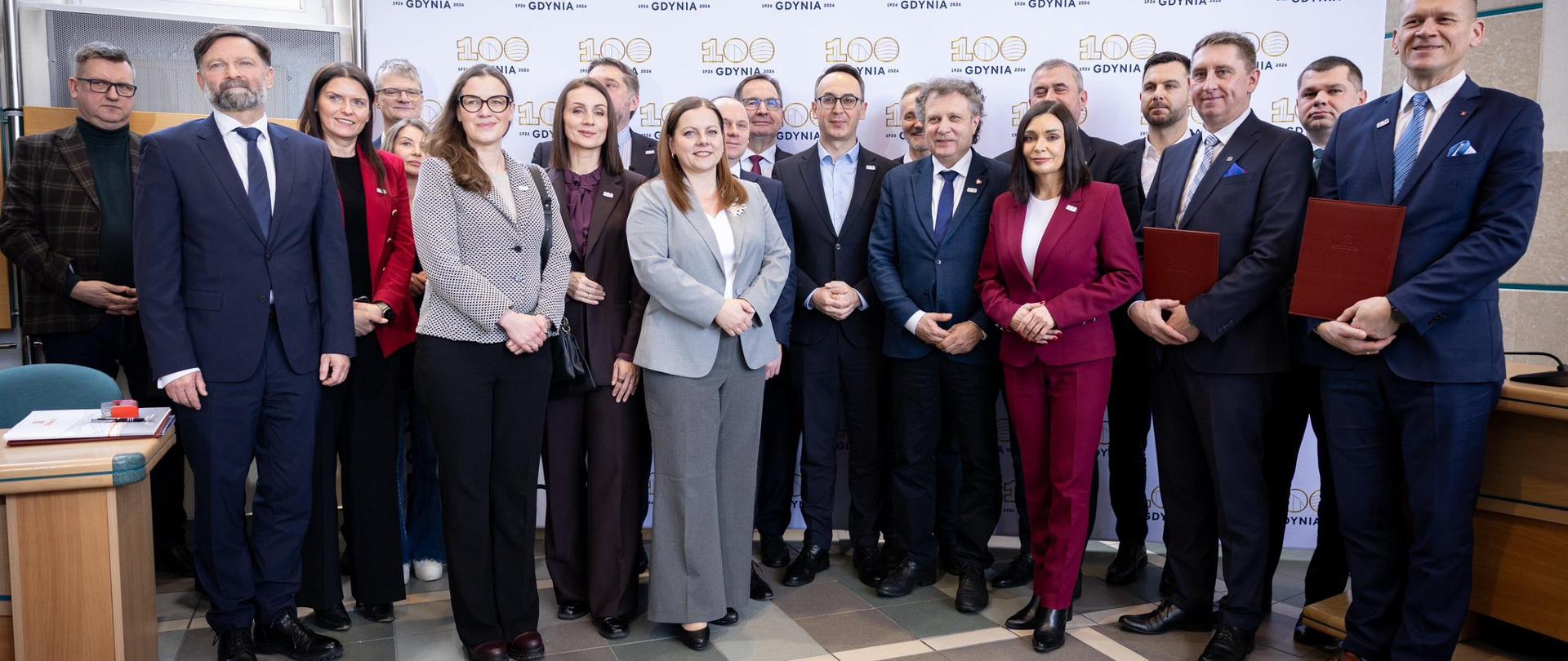 grupa osób stoi na tle baneru 100-lecie Gdyni