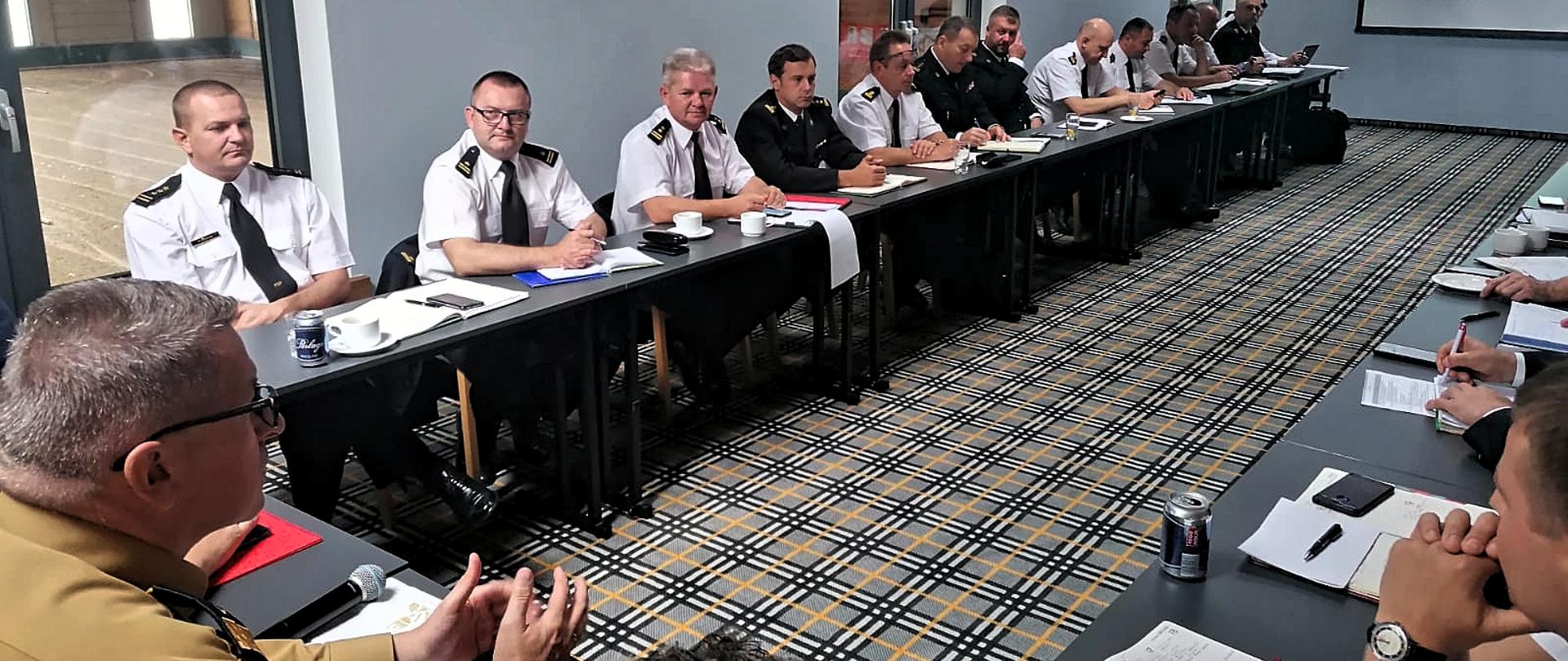 Zastępca Komendanta Głównego nadbrygadier Krzysztof Hejduk oraz uczestnicy narady służbowej siedzą przy stole prezydialnym. 