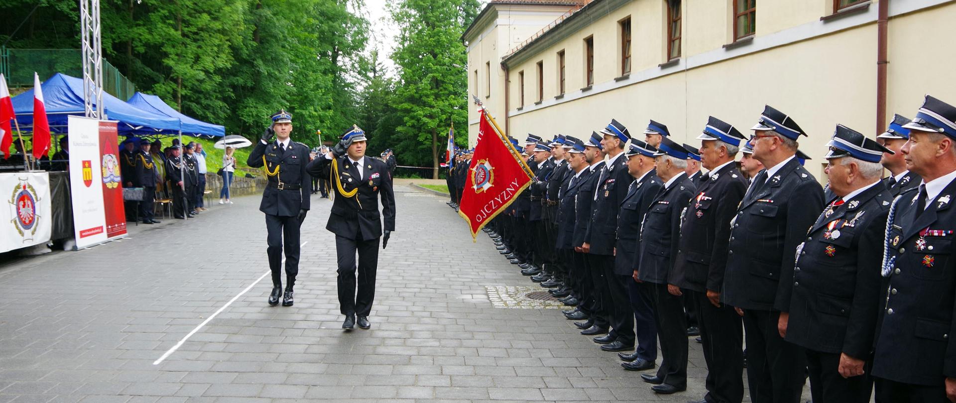 Widok z przodu. Przegląd pododdziałów. Po prawej stronie pododdział OSP. Przeglądu dokonuje Małopolski Komendant Wojewódzki, za nim Dowódca uroczystości. 