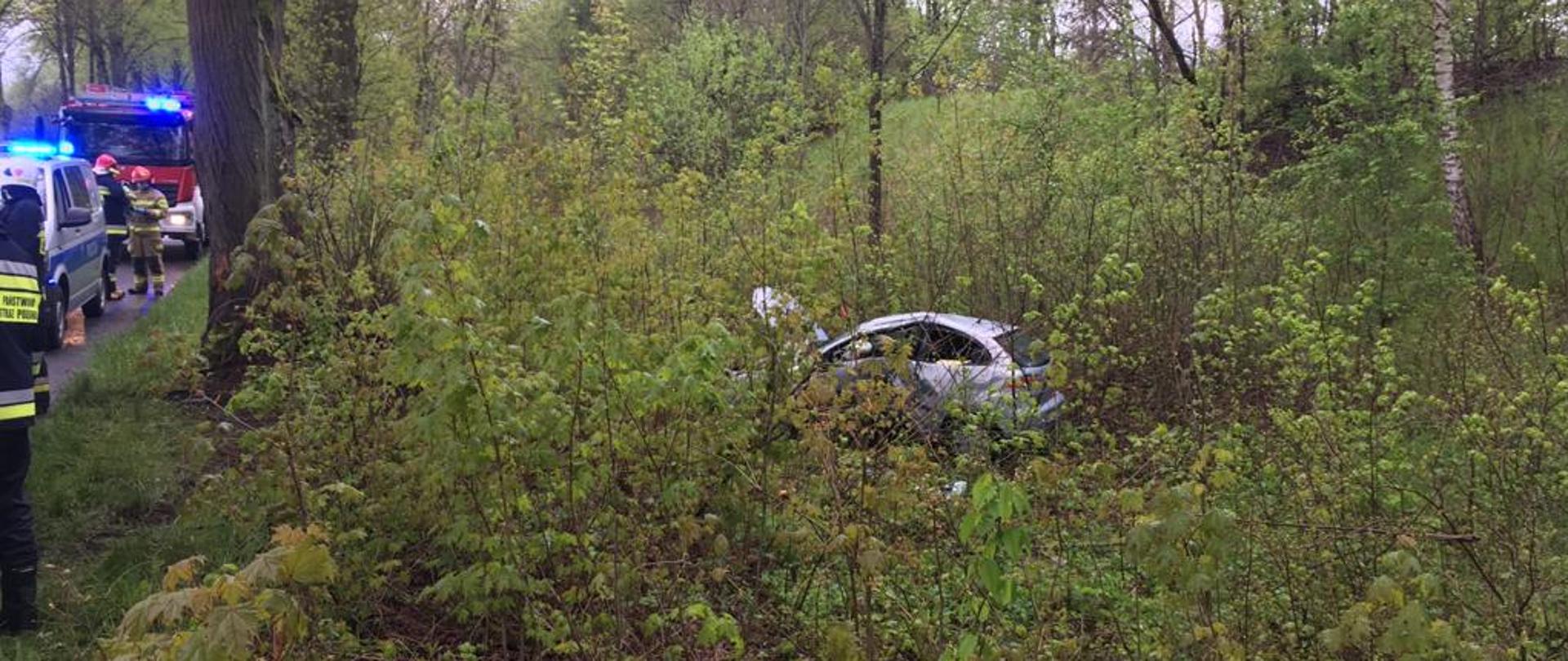 Widok rozbitego samochodu osobowego znajdującego się w lesie obok drogi.