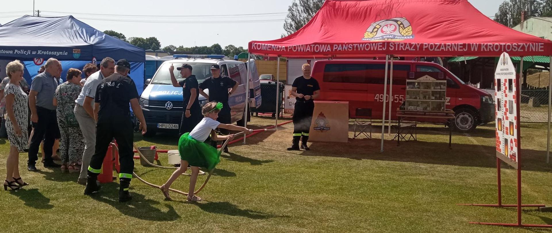 Zdjęcie przedstawia uczestników festynu, którzy gaszą pożar makiety budynku przy pomocy hydronetek. 