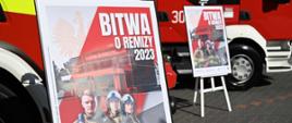 Na zdjęciu widać plakat reklamujący akcję BITWA O REMIZY, w tle wozy strażackie