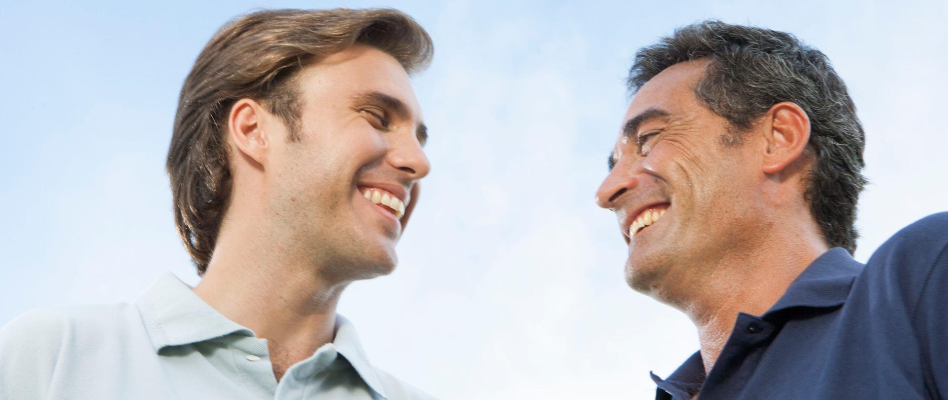 Dwaj mężczyźni - starszy i młodszy - patrzą na siebie, uśmiechają się.