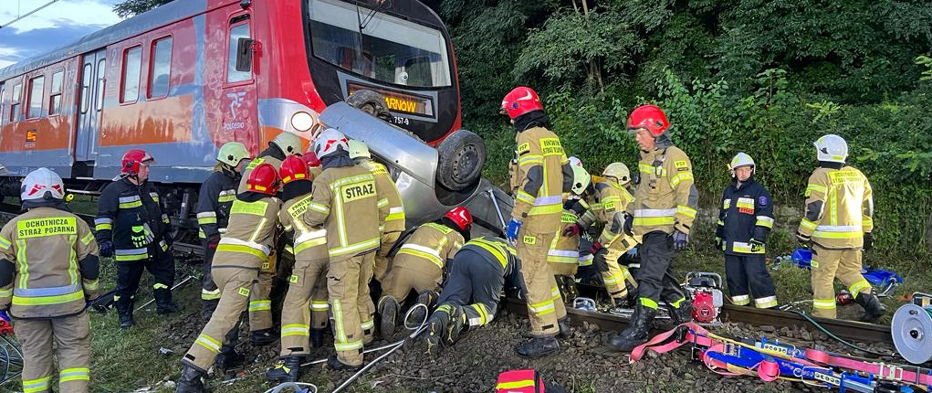 Strażacy prowadza działania przy samochodzie po uderzeniu pociągu