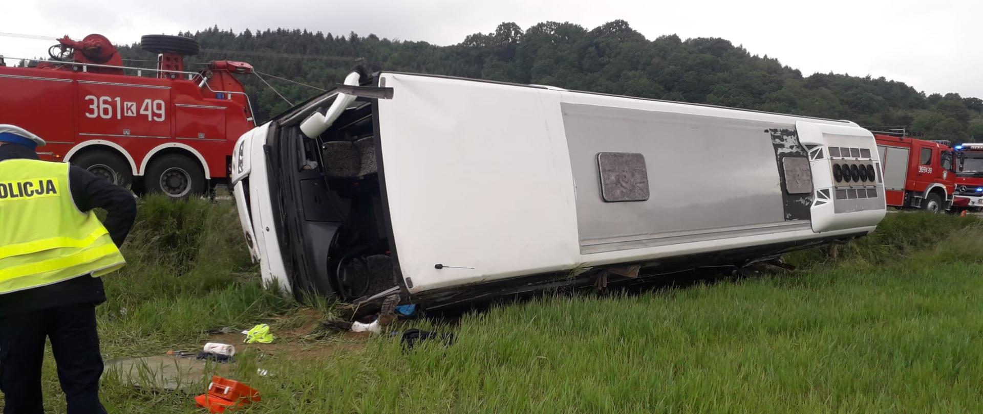 Na zdjęciu widoczny jest autobus w trakcie podnoszenia na koła – działania realizowane są przez samochód ratownictwa drogowego Państwowej Straży Pożarnej.