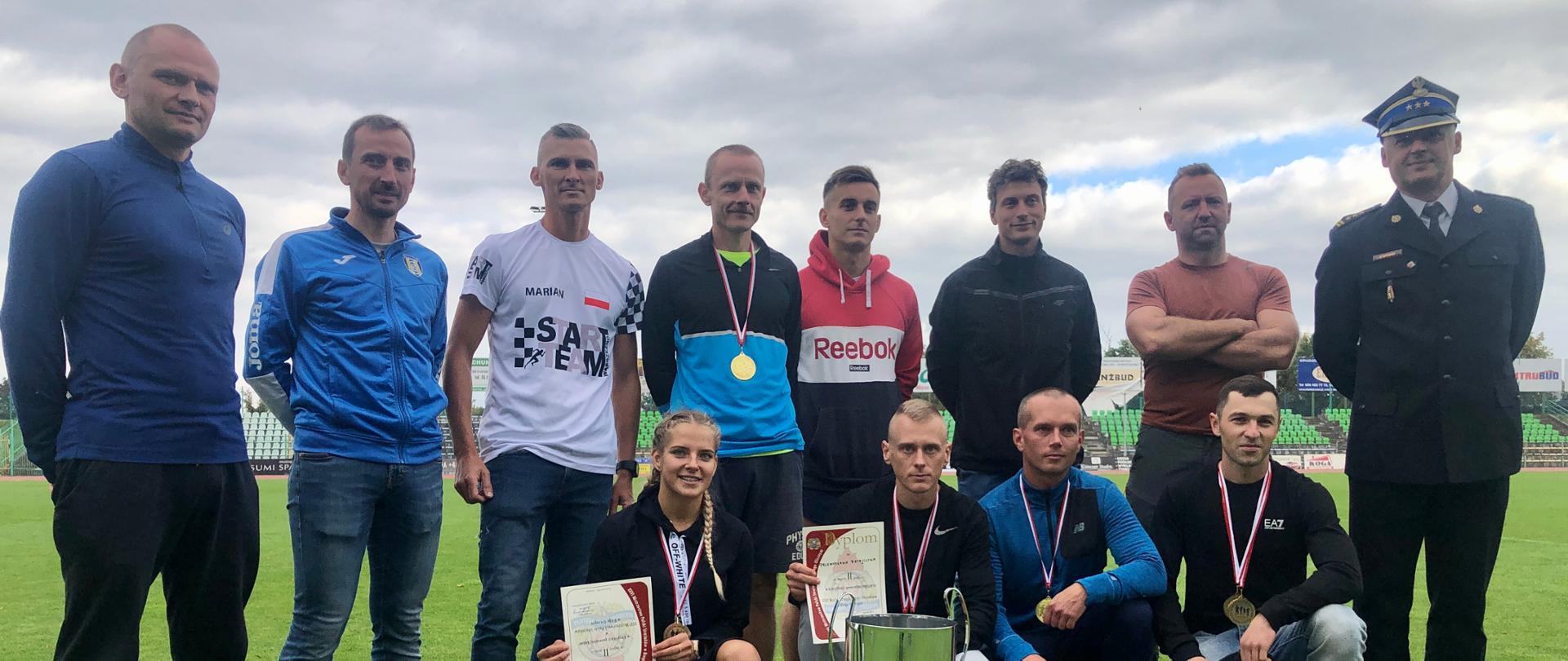 Na zdjęciu widać pozujących biegaczy z dyplomami i medalami obok nich stoi Komendant Miejski PSP z Grudziądza.