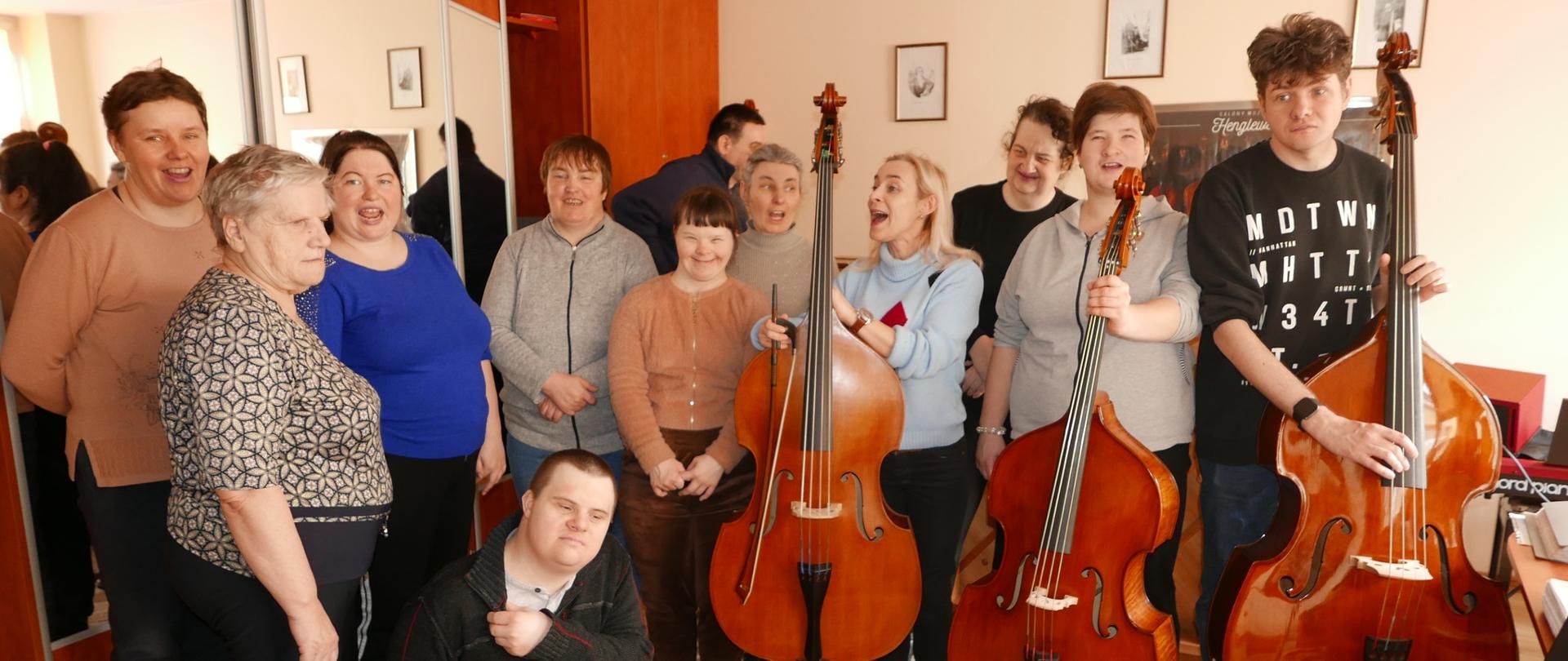 Grupa osób pozująca do zdjęcia. Chłopak, stojąca obok dziewczyna i nauczycielka trzymają kontrabasy.