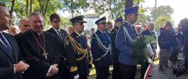Policjant trzyma wiązankę za nim w rzędzie stoją komendant wojewódzki Policji w Gdańsku zastępca pomorskiego komendanta wojewódzkiego Państwowej Straży Pożarnej oraz zaproszeni goście. 