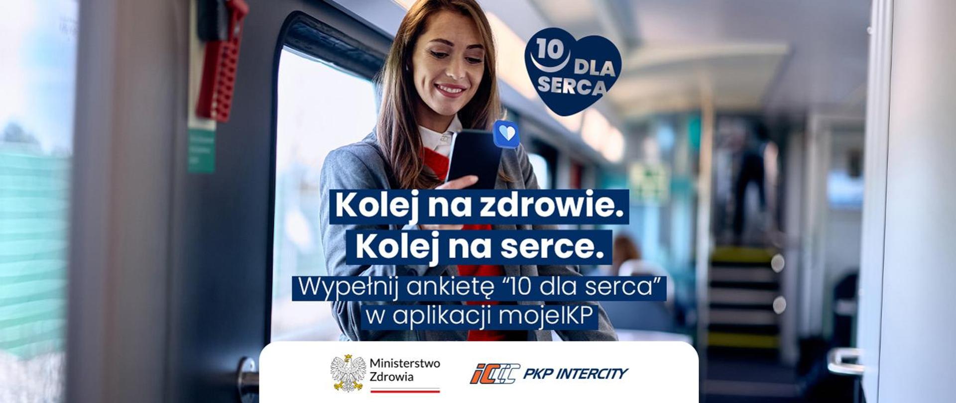 Uśmiechnięta kobieta stoi w wagonie pociągu i korzysta ze smartfona. Na grafice widoczny jest napis „Kolej na zdrowie. Kolej na serce. Wypełnij ankietę ‘10 dla serca’ w aplikacji mojeIKP” oraz logotypy Ministerstwa Zdrowia i PKP Intercity