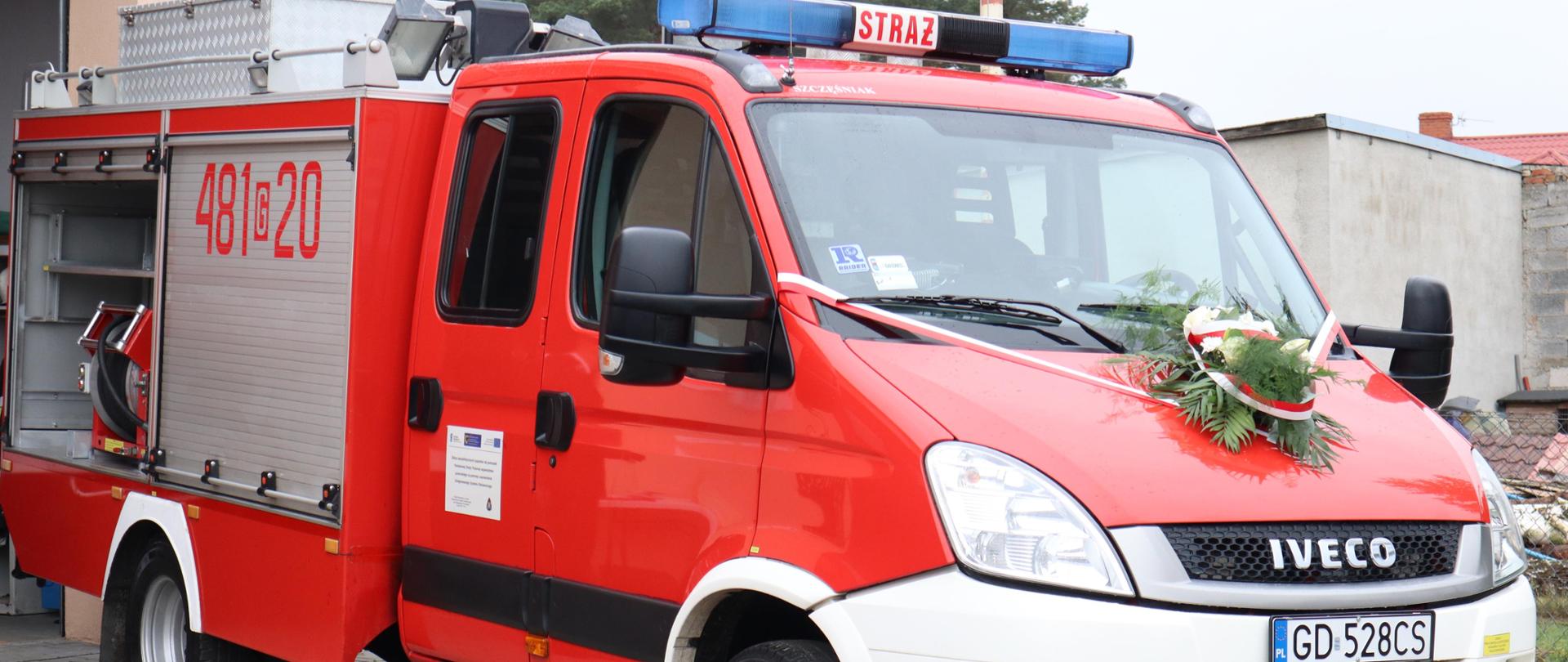 Na zdjęciu przekazywany pojazd pożarniczy, ozdobna wiązanka na masce samochodu