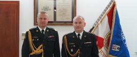 dwóch strażaków w mundurach stoi obok siebie, w tle sztandar